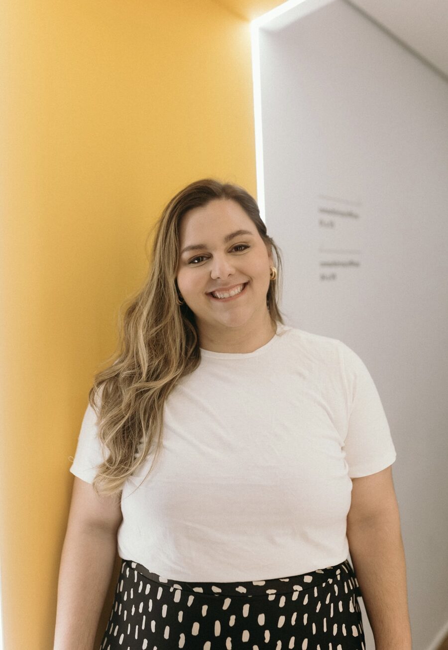Dra. Julia Cunha, pediatra no Rio de Janeiro, sorrindo diante de uma parede amarela